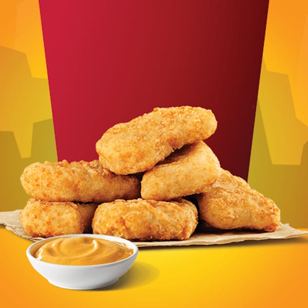 A pile of golden-brown chicken nuggets on parchment paper, with a side of dipping sauce.