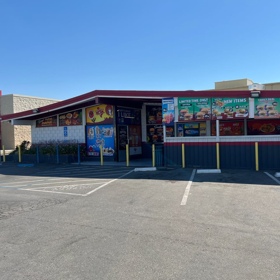 Exterior of Texas Burger Drive-In with a red roof, large menu boards, and an empty parking lot.