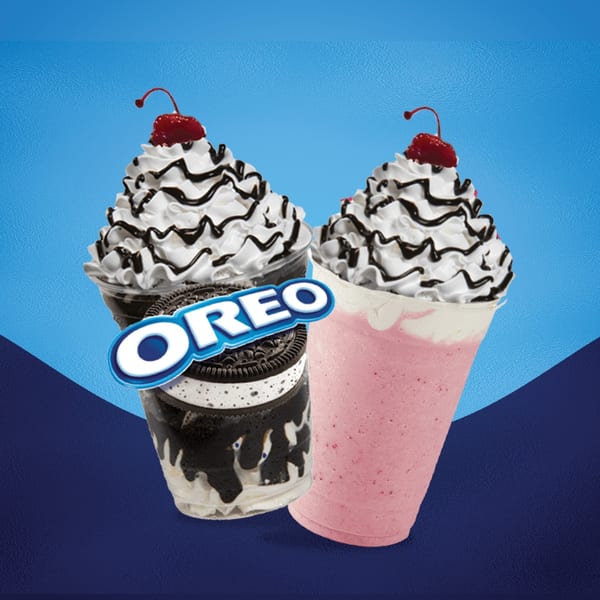 Two Texas Burger Drive-In milkshakes, one Oreo and one strawberry, topped with whipped cream and cherries.