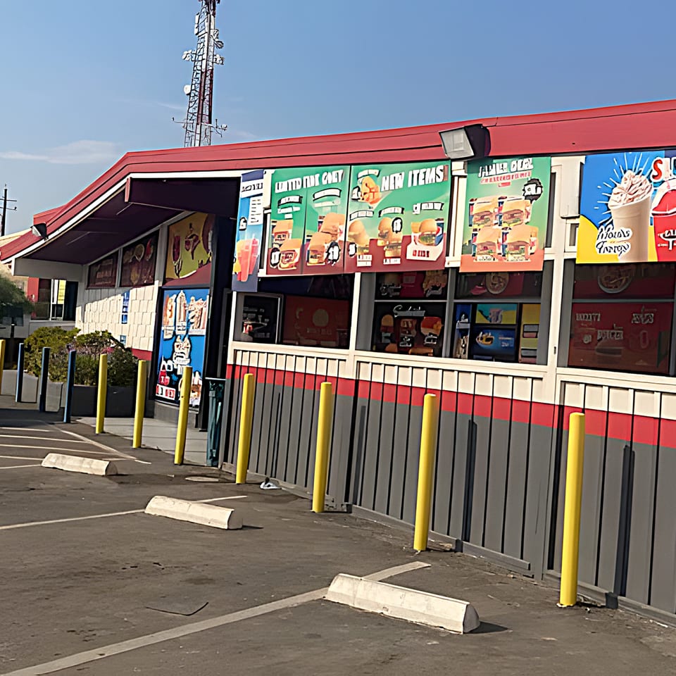 Exterior of Texas Burger Drive-In with a red roof, menu boards, and a parking lot with yellow poles.